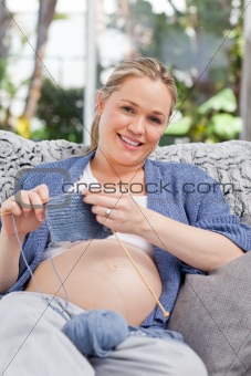 Pregnant woman knitting on her sofa
