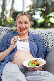 Pregnant woman eating vegetables on her sofa