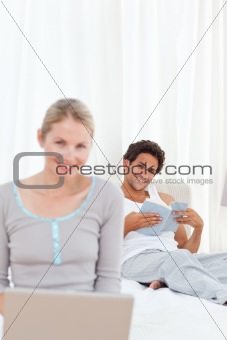 Woman working on her laptop while her husband is reading 