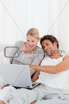 Adorable couple looking at their laptop on the bed 