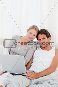 Adorable couple looking at their laptop on the bed 