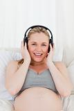 Lovely pregnant woman listening to music on her bed