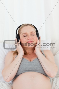 Lovely pregnant woman listening to music on her bed