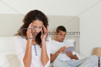 Woman having a headache while her husband is reading