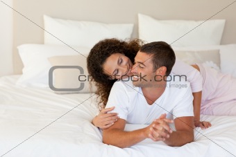 Pretty woman hugging her husband on their bed at home