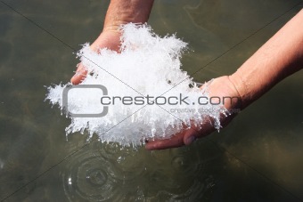 Hand holding salt crystals from salt lake above the water surface