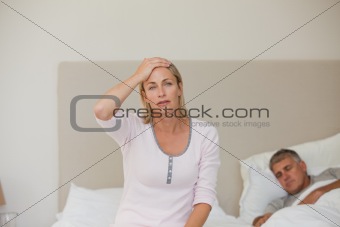 Woman having a headache while her husband is sleeping