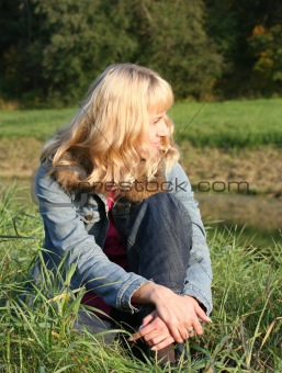 young blond woman is sitting on a grass