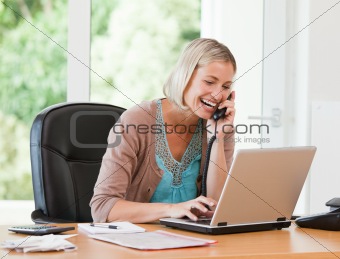 Woman working on her computer while she is phoning