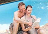 Couple reading a book beside the swimming pool
