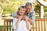 Elderly man hugging his wife who is on the bench