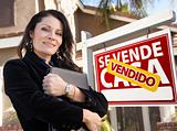 Proud, Attractive Hispanic Female Agent In Front of Spanish Vendido Se Vende Casa Real Estate Sign and House.