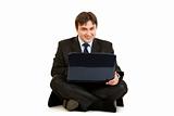 Smiling  businessman sitting on floor and working on laptop
