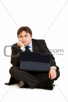 Bored businessman sitting on floor with laptop
