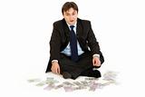 Prosperous businessman sitting on floor surrounded by money
