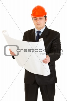 Serious businessman in helmet holding building plan in hand
