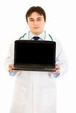 Serious  doctor holding laptop with blank screen in hands
