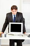 Modern businessman standing at office desk and looking in monitors blank screen
