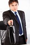 Authoritative businessman standing at office desk and giving briefcase. Close -up. 
