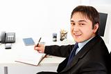 Smiling  businessman sitting at office desk and planning timetable in diary
