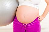 Pregnant woman in sportswear holding fitness ball. Close-up.
