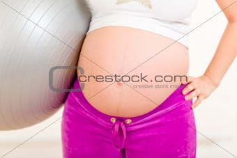 Pregnant woman in sportswear holding fitness ball. Close-up.
