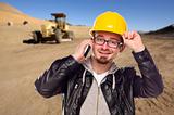Young Cunstruction Worker on Cell Phone in Dirt Field with Tractor in the Background.