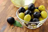 black and green olives and a bottle of olive oil on brown board