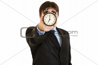 Businessman holding alarm clock in front of face. Focus on alarm clock 
