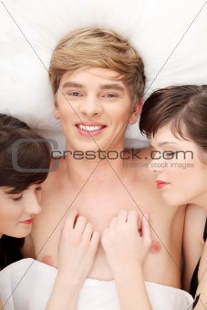 Handsome man lying in bed with two girls 