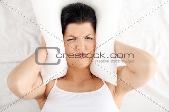 Female lying on bed and closing her ears with pillow 