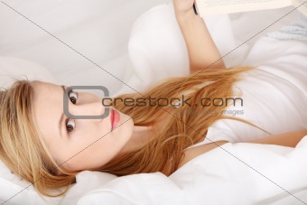 Young blond woman reading book on the bed