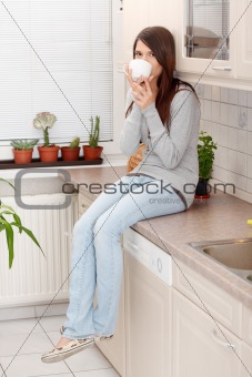 Young woman having coffee or tea in the kitchen 