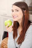 Woman in kitchen eating green apple