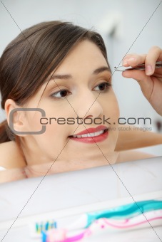 Young woman plucking her eyebrows