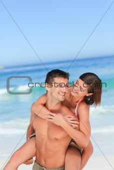 Handsome man having wife a piggyback on the beach