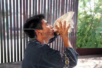 Mayan man blowing seashell as horn in jungle
