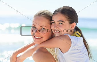 Mother having her daughter a piggyback at the beach