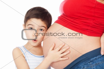 Surprised boy holding mother's belly with hands and listening