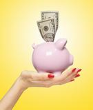 piggy bank with dollars on woman hand over yellow