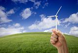 Male Fist Holding Wind Turbine Outside with Grass Field, Sky and Clouds.