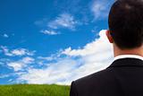 View of Businessman's back and  watching blue sky and green field