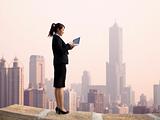 Businesswoman using computer and  stand on the top of a skyscraper with cityscape