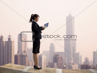 Businesswoman using computer and  stand on the top of a skyscraper with cityscape