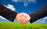 Close-up of a business people shaking hands against blue sky and green background