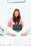 Concentrated pretty woman sitting on sofa  and using laptop
