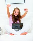 Excited woman sitting on sofa with laptop and rejoicing her success 
