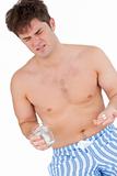 Bare-chested man in pajamas holding pills and a glass of water