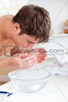 Bright caucasian man spraying water on his face after shaving in