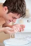 Smiling caucasian man spraying water on his face after shaving i